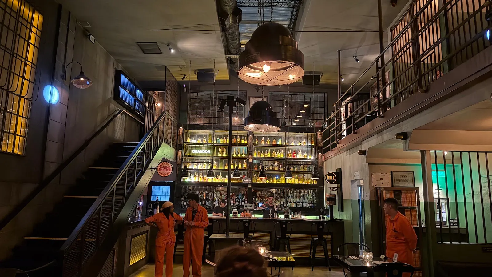 Salón principal con barra, entrepiso y botellas iluminadas